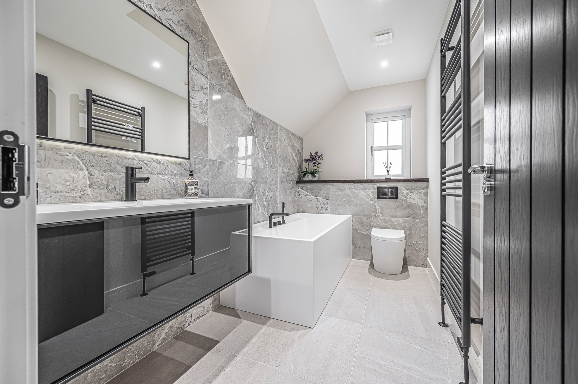 Ensuite bathroom finished in grey marble tiling with a freestanding bath and black fittings