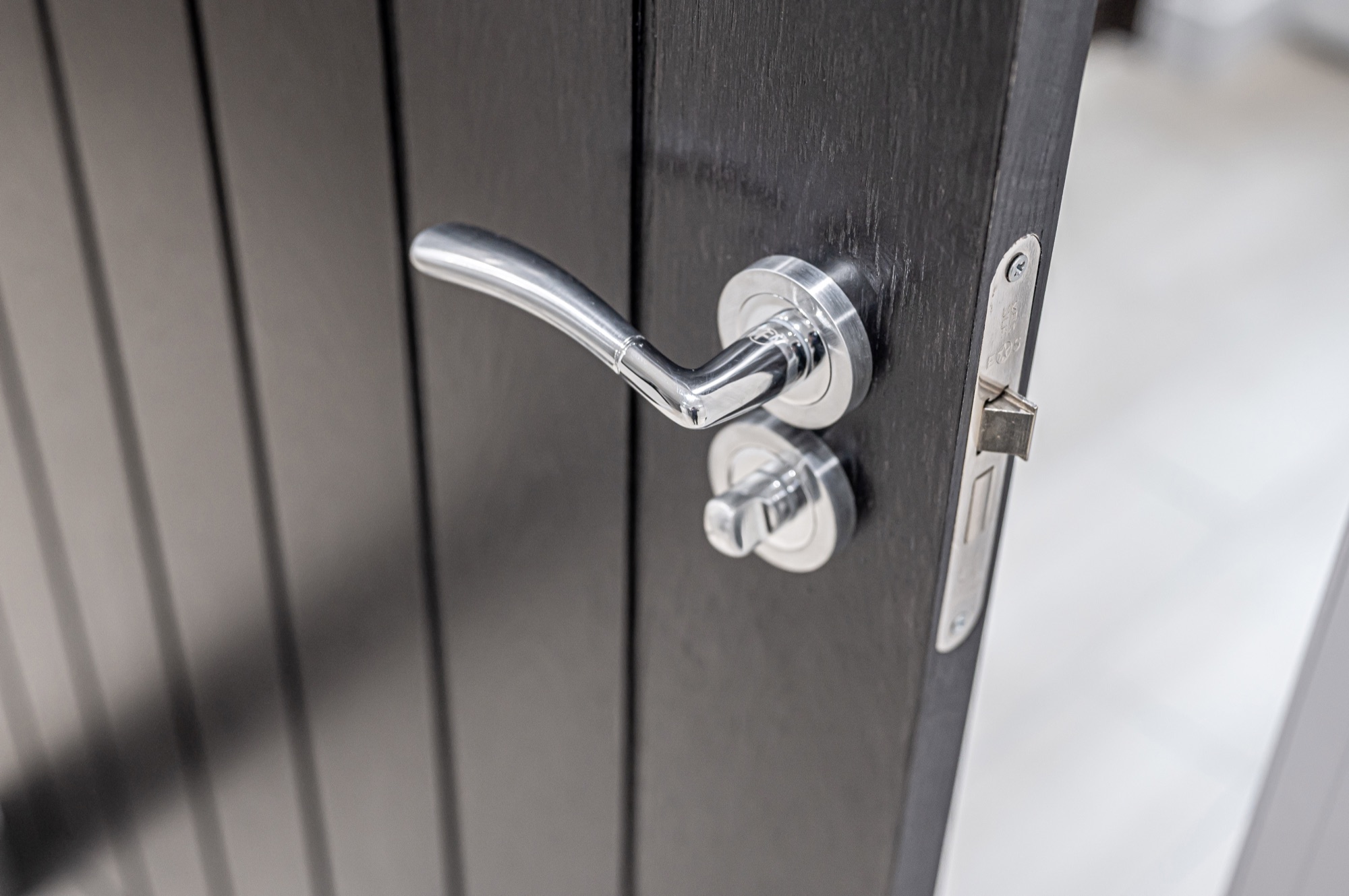 Close-up of a chrome door handle on a dark timber-clad door