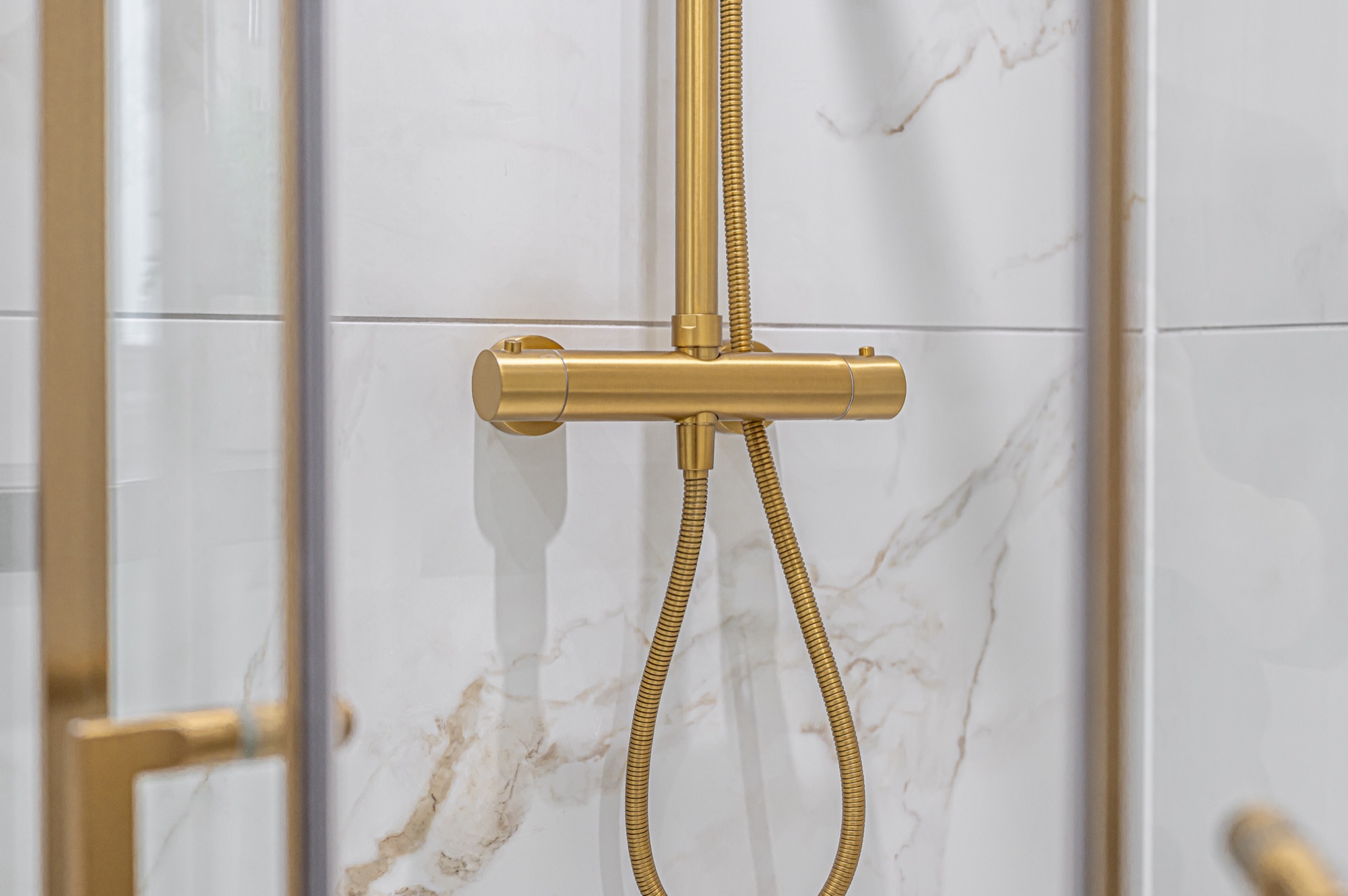 Close-up of a brushed gold thermostatic shower valve against marble tiling