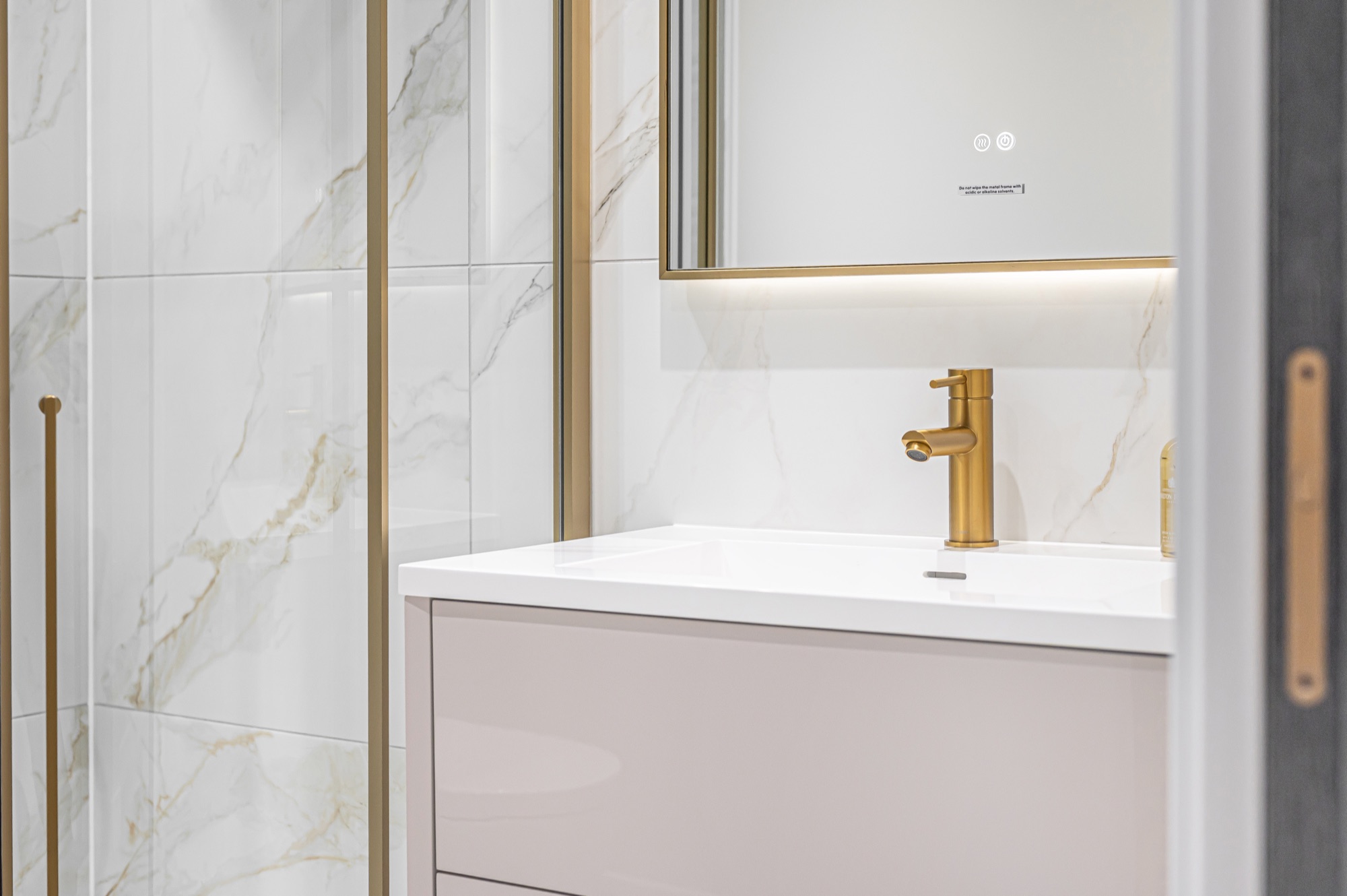 Close-up of a brushed gold vanity tap beside a mirror and orchid