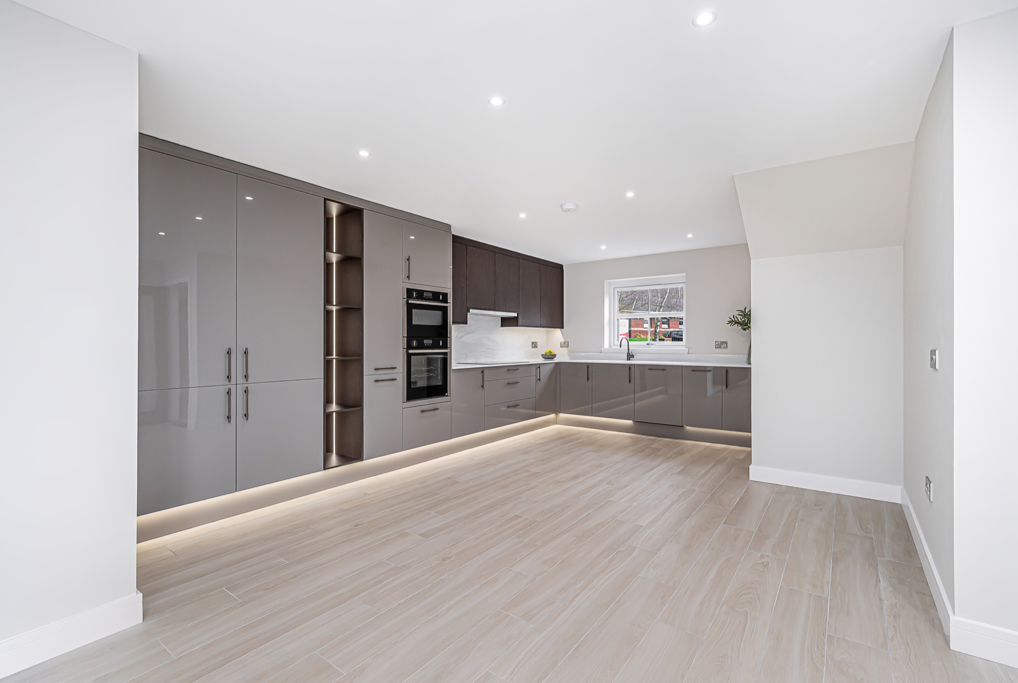Open-plan kitchen with high-gloss grey and dark wood cabinetry, integrated appliances and warm underlighting