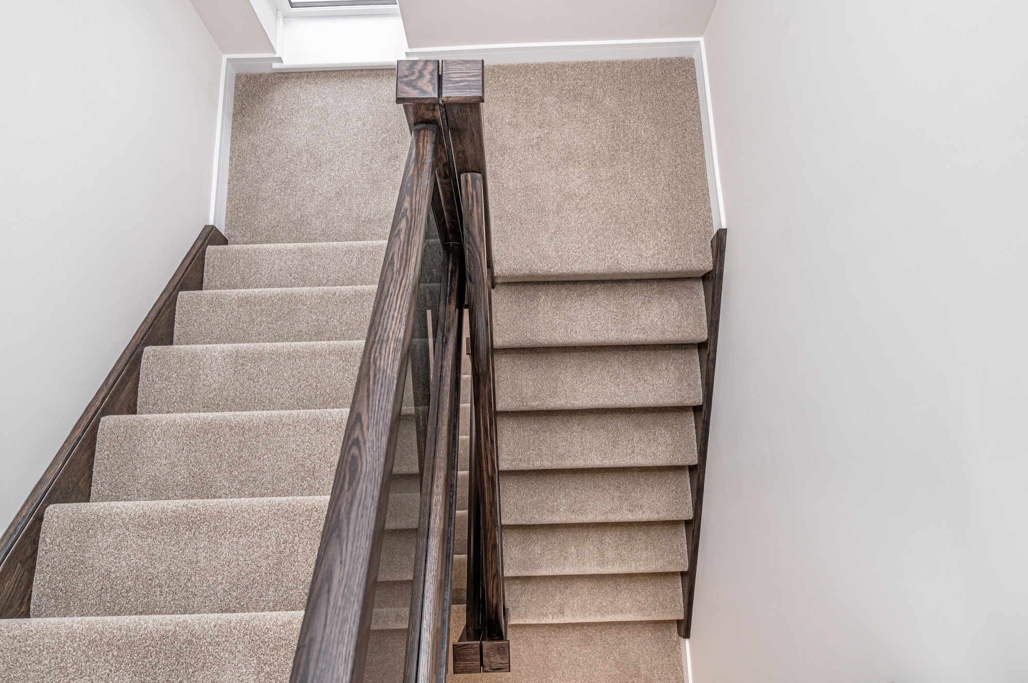Wide view of a staircase with dark timber balustrade and glass panels, looking down from the top floor